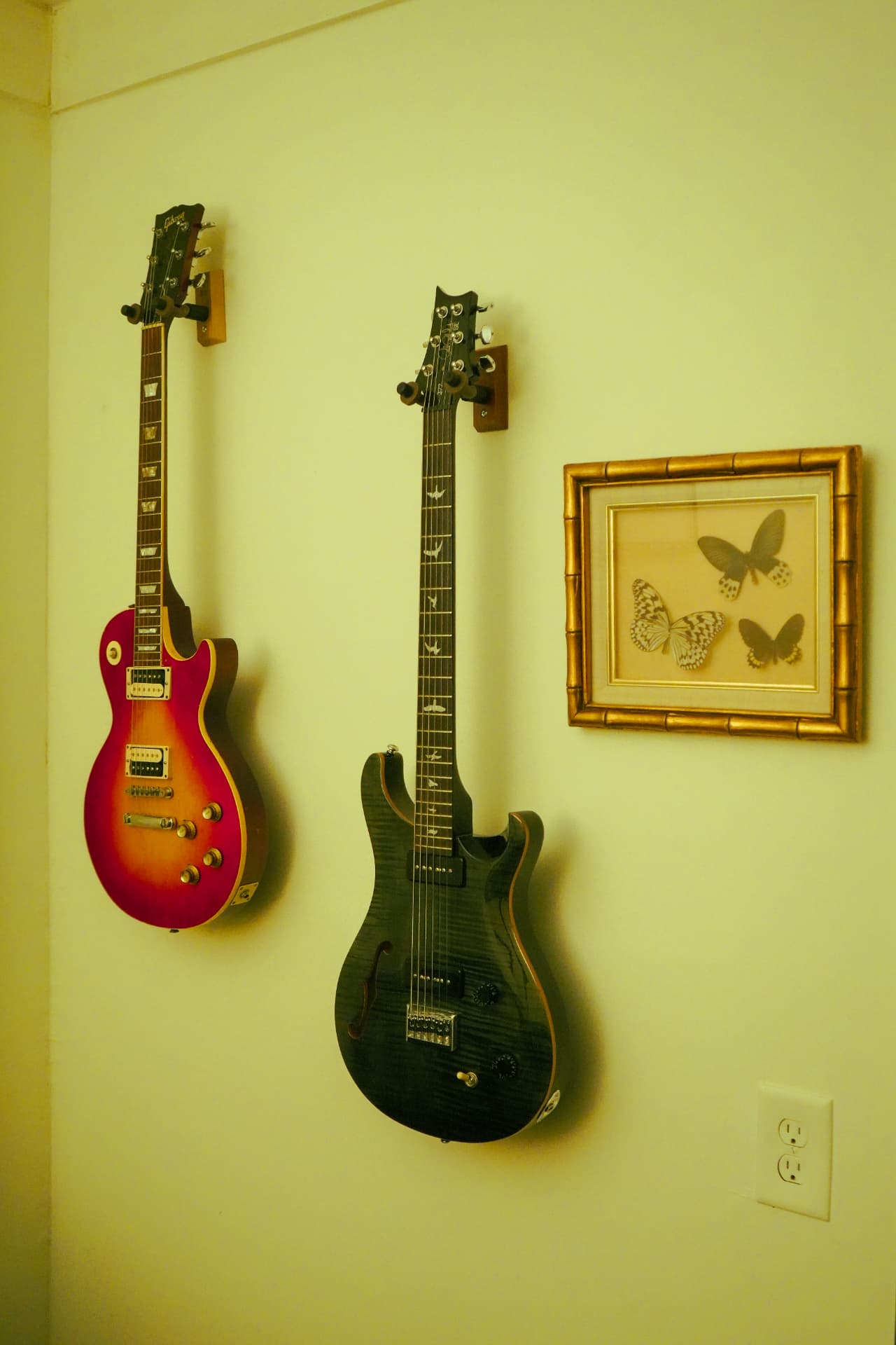 Gibson Les Paul and PRS guitars beside a framed butterfly print